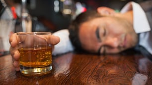 drunk man sleeping on counter with glass of whiskey in hand